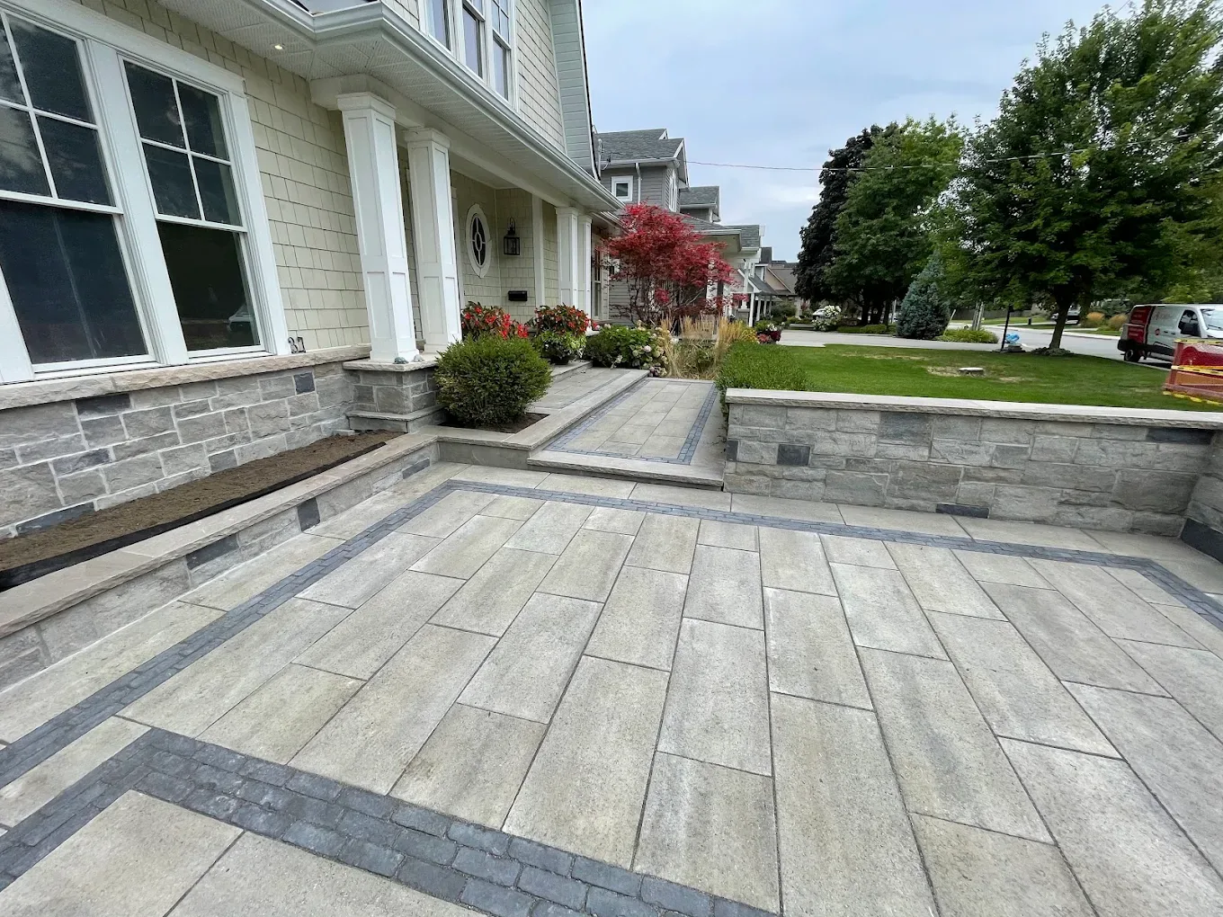 Interlocking front entrance in slab pavers with a charcoal soldier-course border and a natural stone retaining wall