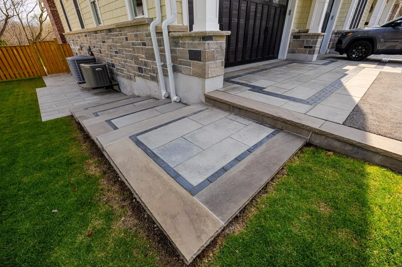 Interlocking side-entrance walkway running past a cedar privacy fence to a raised paver landing